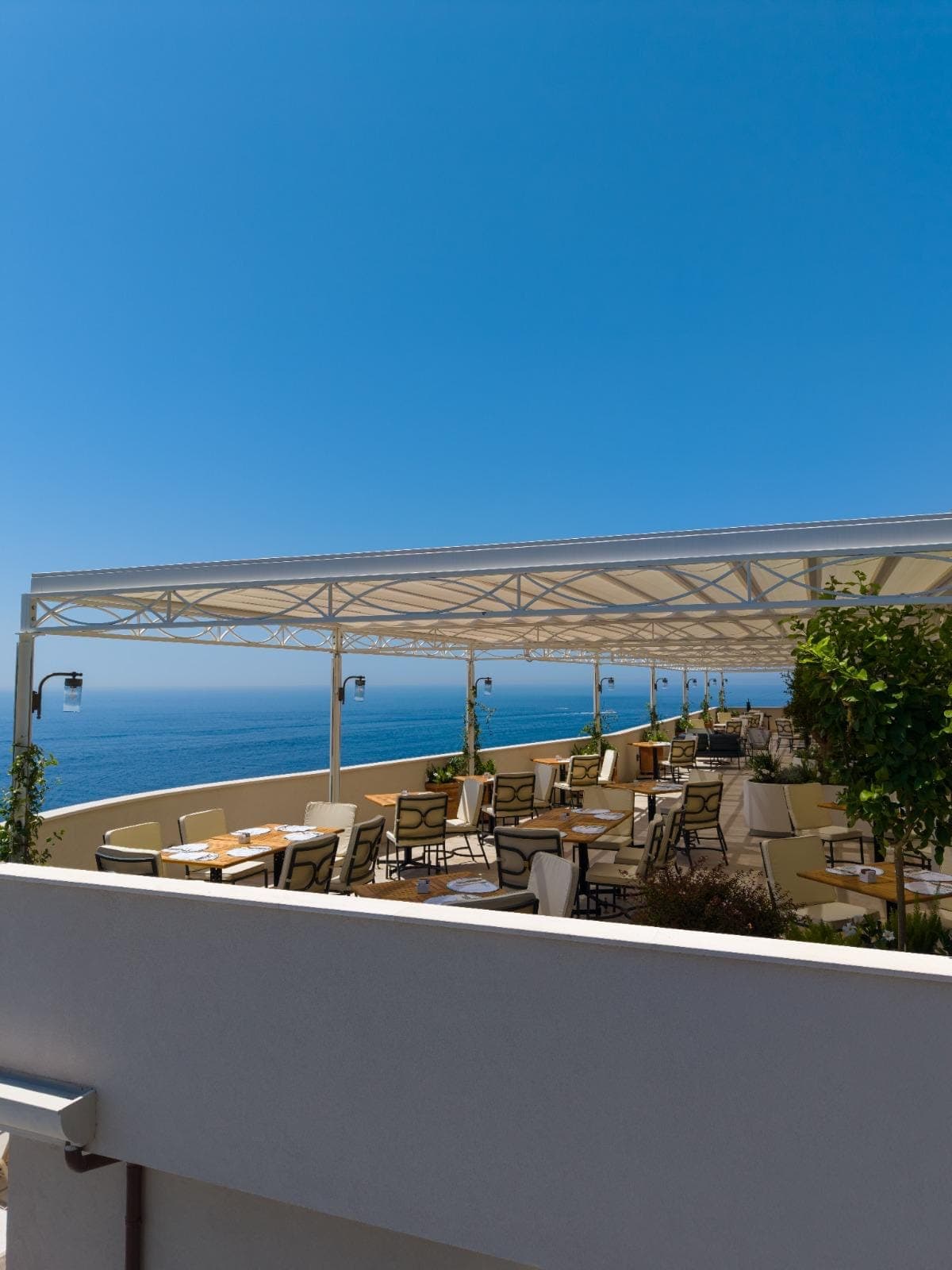 Pergola bianca su misura sulla terrazza dell'hotel, con i tavoli apparecchiati e il mare di Amalfi sullo sfondo
